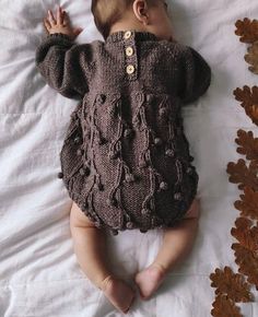 a baby laying on top of a bed wearing a brown knitted sweater and pants