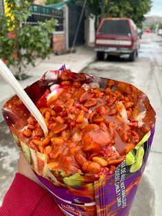 a person holding up a bag of food on the side of the road with a spoon in it