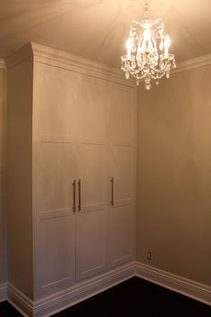 an empty room with white cabinets and a chandelier hanging from it's ceiling