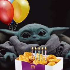 a baby yoda is sitting in front of a box with donuts and balloons