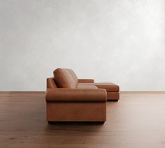 a brown leather couch sitting on top of a hard wood floor next to a white wall