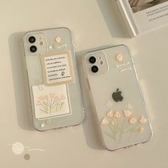 two iphone cases sitting on top of a table next to an open book and phone case