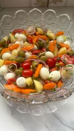 a glass bowl filled with lots of different types of vegetables on top of a table