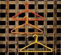 two colored clothes hangers sitting on top of a wooden fence next to each other