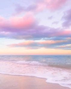 an ocean beach with waves coming in to shore and pink clouds above the water at sunset