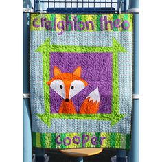 a colorful quilt hanging on the side of a blue metal rack with an orange and white fox