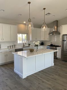 a large kitchen with white cabinets and an island in the middle, surrounded by stainless steel appliances