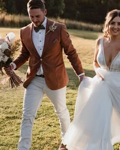 a bride and groom are walking through the grass holding hands with each other in their wedding attire