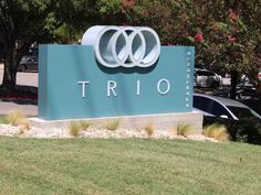 a large sign that says trio in front of some trees and cars parked on the street