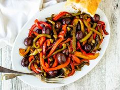 a white plate topped with olives, peppers and bread