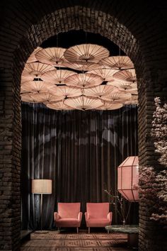 two pink chairs sitting in front of an arch with umbrellas hanging from the ceiling