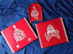 three red boxes with white designs on them sitting on a blue sheet covered bed next to each other