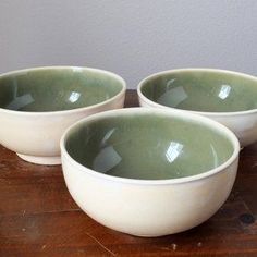 three white bowls sitting on top of a wooden table next to each other with green rims