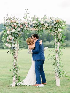 a bride and groom kissing under an outdoor wedding ceremony arch with greenery on the side