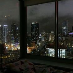 a view of the city at night from a bedroom in a skyscraper building, looking out over a large city