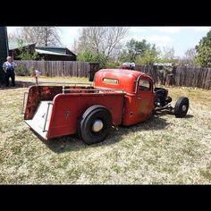 an old red truck is parked in the yard with two men standing around behind it