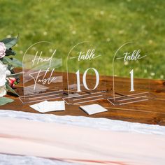 two clear acrylic table numbers sitting on top of a wooden table with flowers