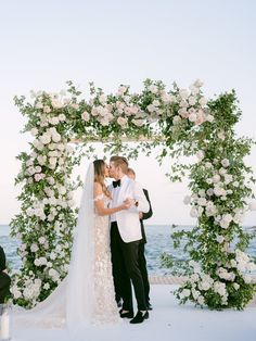 a bride and groom standing under an arch with white flowers on it at the end of their wedding ceremony