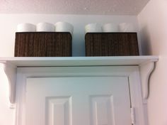 two brown baskets on top of a white door with toilet paper rolls in the bottom