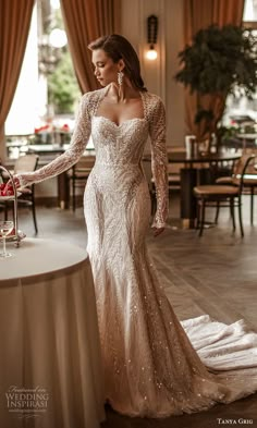 a woman in a long sleeved wedding dress standing next to a table with wine glasses on it