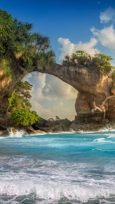 an arch in the rock over looking the ocean with waves coming up from underneath it