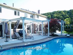 an outdoor pool with chairs and umbrellas next to a large white house in the background