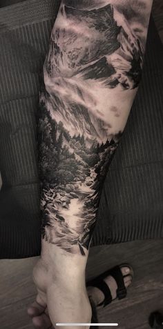 a man's arm with a mountain scene on it and clouds in the sky