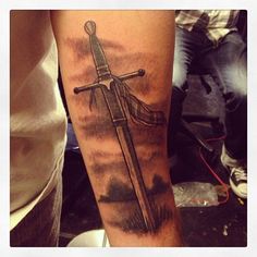 a man's arm with a cross tattoo on it and clouds in the background