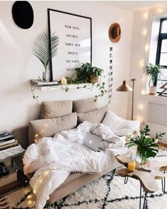 an unmade bed in a white room with plants on the headboard and lights hanging from the ceiling