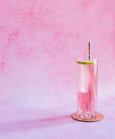 a glass filled with liquid and a straw sticking out of the top, on a pink background