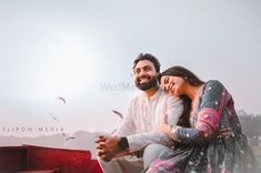 a man and woman sitting on the back of a red boat with seagulls flying overhead