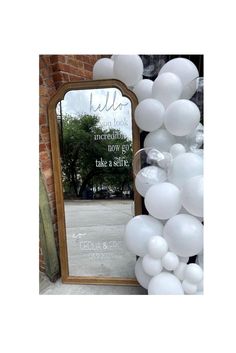 a mirror and some white balloons on the ground next to a brick wall with a sign that says hello