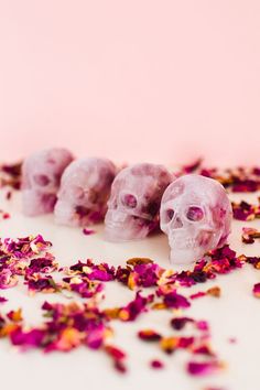 three sugar skulls surrounded by pink flowers on a white surface with petals scattered around them