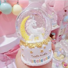 a hand holding up a snow globe with a unicorn on it in front of other decorations