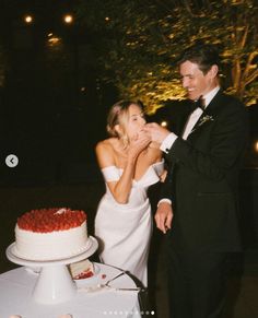 a man and woman standing next to each other in front of a cake