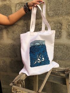 This tote features originality in design, concept and thought. Embrace the Artistic Fusion: Fankar (فنکار) Hand-Painted Tote - Where Cultures Converge. This stunning masterpiece transcends language barriers, blending the allure of Urdu calligraphy with the universal language of art. With each brushstroke, Fankar comes to life, imbuing the fabric with the rich essence of creative expression. This hand-painted tote is not only a cherished possession for artists; it is a symbol of unity and appreci Rectangular Bags With Artwork For Daily Use, Everyday Artwork Tote Bag, Artsy Everyday Bags With Artwork, Everyday Tote Bag With Artwork, Artistic Square Bags For Everyday, Artistic Rectangular Shoulder Bag With Artwork, Artwork Tote Bag For Artistic Expression, Artistic Square Bags For Daily Use, Artistic Square Bag For Daily Use