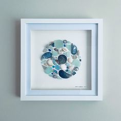 a white frame with blue and green sea glass in the shape of a circle on it