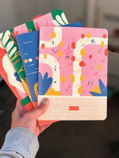 a person holding five notebooks in their hand, each with different designs on them