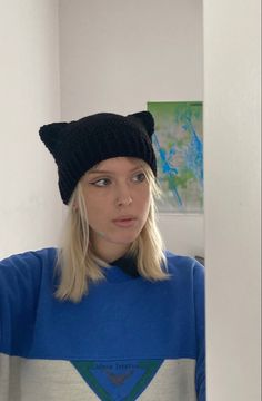 a woman with blonde hair wearing a blue sweater and a black cat hat is looking at the camera