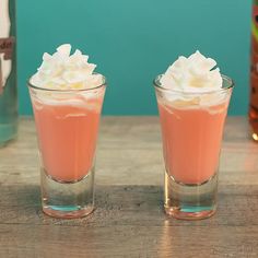 two shot glasses filled with whipped cream on top of a wooden table