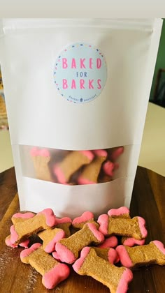 pink and brown dog biscuits in front of a bag on a wooden table with a sticker that says baked for bakes