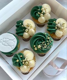 four cupcakes with green and white frosting in a box on a table