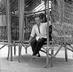 a man sitting on top of a wooden bench next to a bamboo structure covered in branches