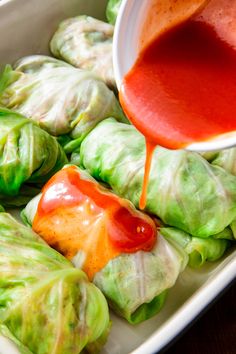 some lettuce rolls with sauce being drizzled onto them and sitting on a plate