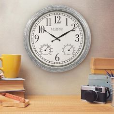 a clock that is on the side of a wall next to some books and a cup