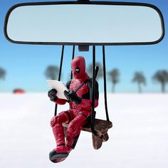 a deadpool figurine sitting on a swing in front of a rear view mirror