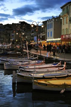 many small boats are docked in the water near some buildings and people walking on the sidewalk