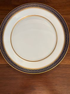 an empty white plate with blue and gold trim on a wooden table top, ready to be used as a serving platter