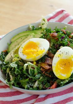 a salad with hard boiled eggs and bacon in it on a red and white striped napkin