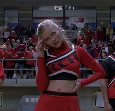 two cheerleaders are standing in front of a crowd and one is talking on her cell phone